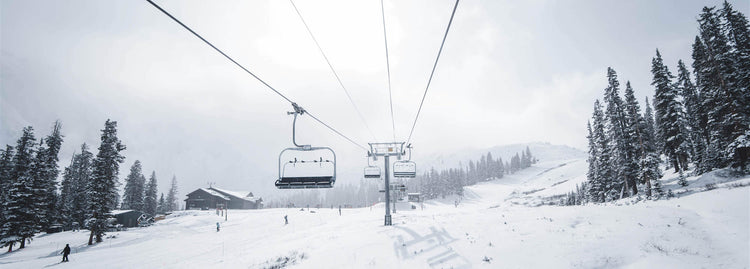 Ski lift in a snowy mountain landscape with trees and a building.